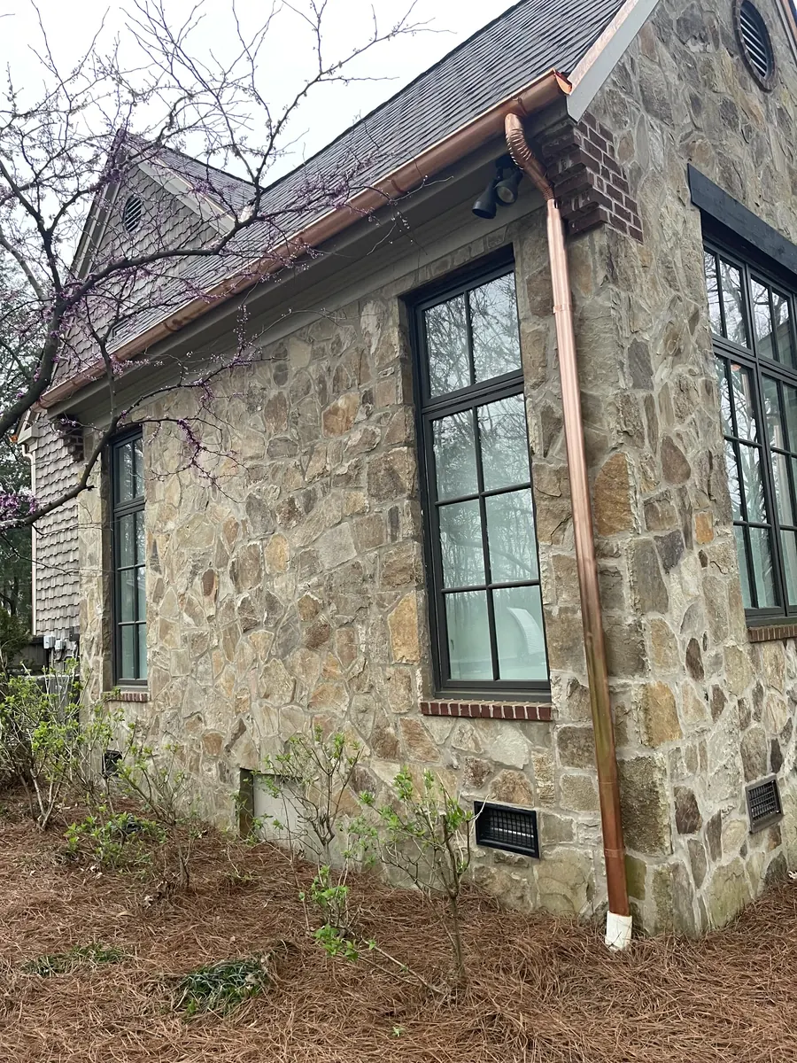 Copper half-round gutter and downspout on a stone home, installed by Three Stone