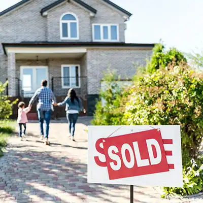 Home For Sale sign covered by the word Sold, and a happy family running to their new home